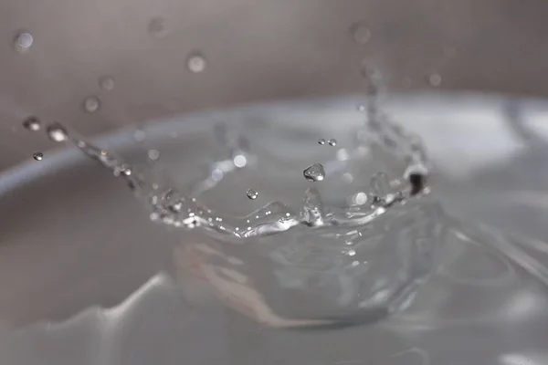 Wassertropfen fallen auf die Oberfläche eines mit Flüssigkeit gefüllten Glases. — Stockfoto