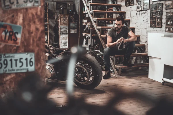 Motociclista sentado em escadas na oficina — Fotografia de Stock