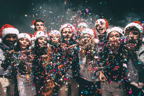 Mensen in Santa hoeden waait confetti — Stockfoto