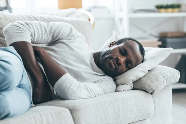 Mies makaa sohvalla ja koskettaa vatsaa — kuvapankkivalokuva