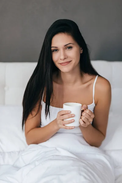 Wunderschöne Frau hält Tasse im Bett — Stockfoto