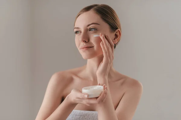 woman spreading cream on face