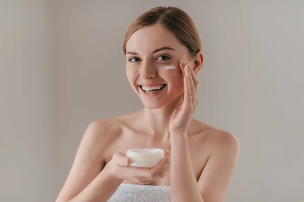 Woman spreading cream on face — Stock Photo, Image