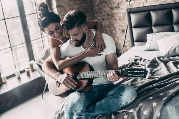 Пара с акустической гитарой в постели — стоковое фото
