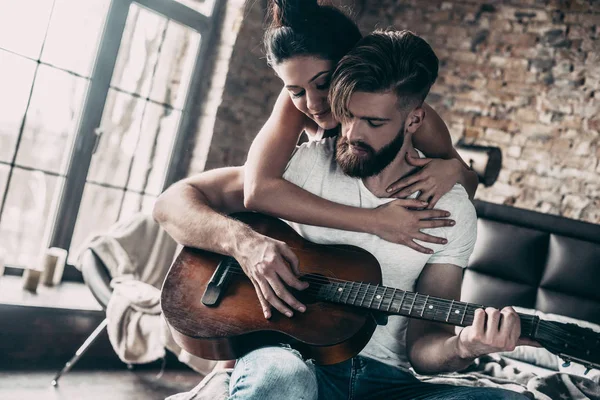 Пара с акустической гитарой в постели — стоковое фото
