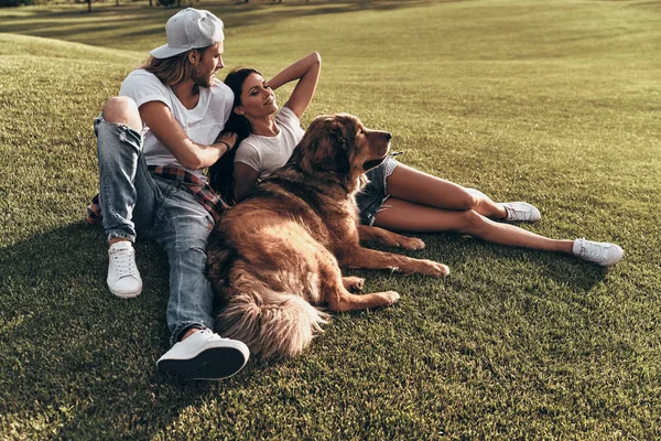 Pareja acostada en la hierba con perro — Foto de Stock