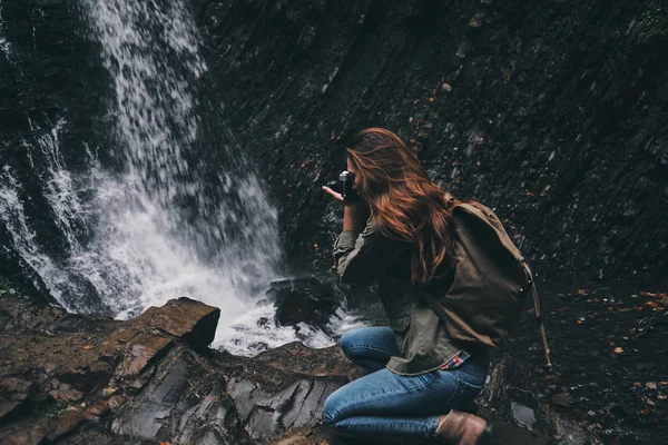 Женщина фотографирует водопад в горах — стоковое фото