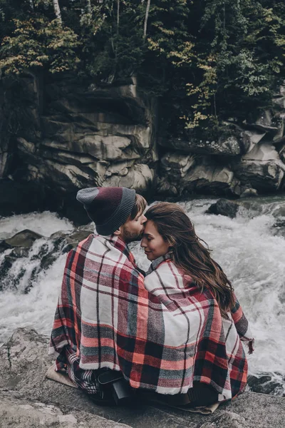 Casal coberto com cobertor sentado em rochas — Fotografia de Stock