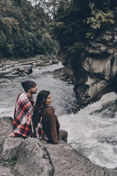 Casal coberto com cobertor sentado em rochas — Fotografia de Stock