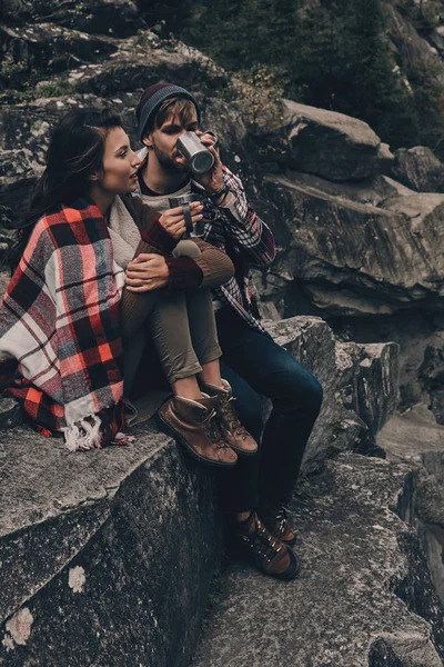 Couple covered with blanket sitting on rocks — Stock Photo, Image