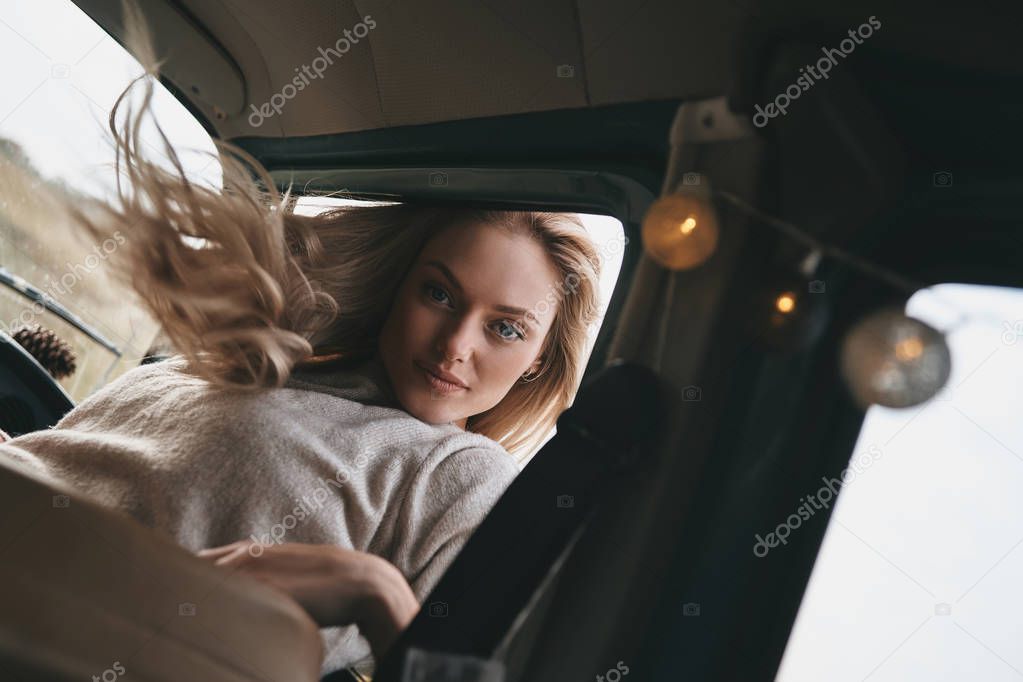 beautiful blonde young woman sitting in car and looking at camera