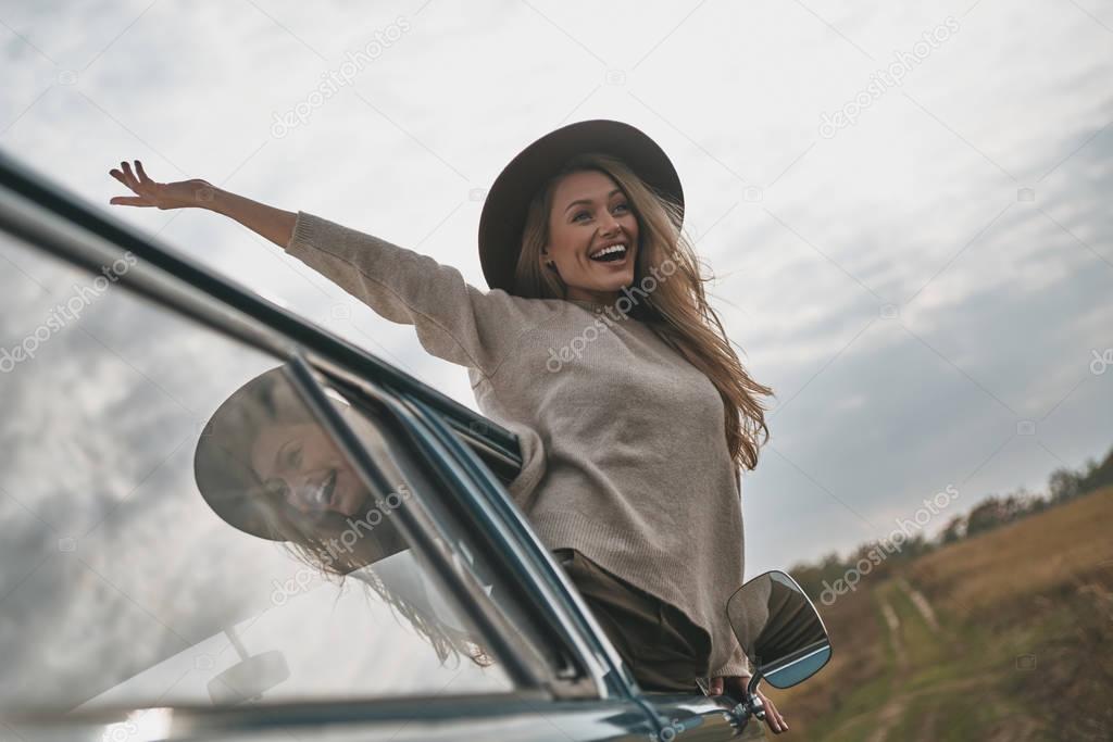 Attractive young woman leaning out of van car window and keeping arms outstretched while enjoying car travel