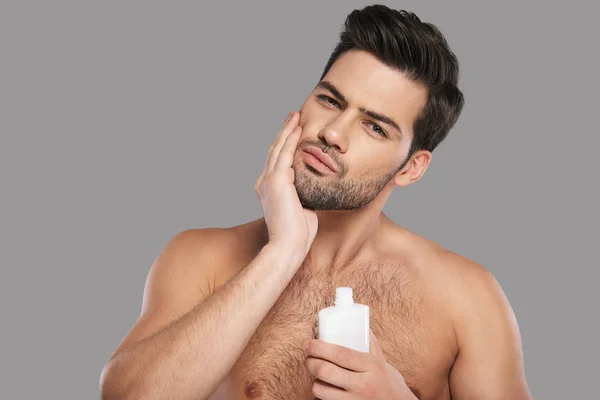Stilig Ung Man Tillämpa Aftershave Lotion Och Ständiga Mot Grå — Stockfoto