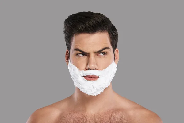 Confused young man with foam on face looking away, ready to shave stubble