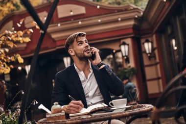 Yakışıklı genç adam akıllı telefonda konuşurken ve günlük müşteri gereksinimleri yazı
