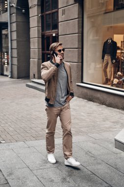 Casual yakışıklı adamın tam uzunlukta giymek akıllı telefonda konuşurken ve şehir sokak yürüyüş