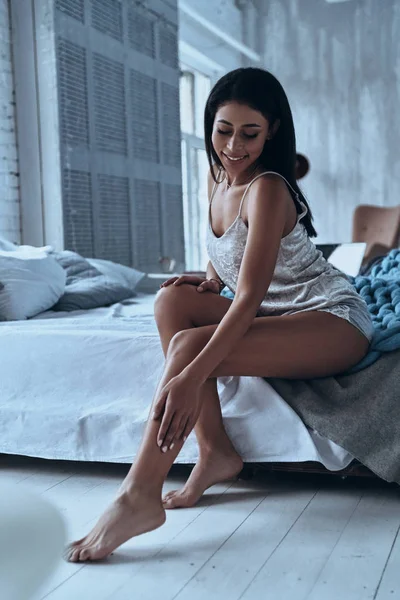 Приваблива Брюнетка Молода Жінка Посміхається Торкається Ноги Сидячи Ліжку Вдома — стокове фото