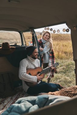 Yakışıklı genç adam kadın car yakınındaki bir şarkı dinleme sırasında gitar çalmak