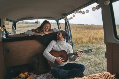 genç adam sevgilisini retro tarzı mini van araba ile Dekoratif ışıklar garland için akustik gitar çalmak