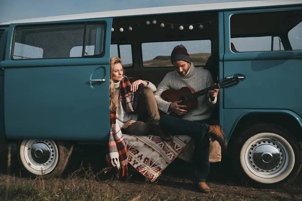 man playing new song on acoustic guitar for his girlfriend in blue retro style mini van car