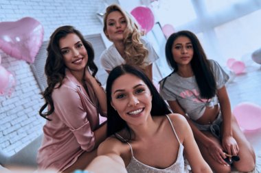 Gülümseyen ve balonlar ile yatak odasında otururken kameraya bakarak pijama dört çekici genç kadınların kendi kendine portre 