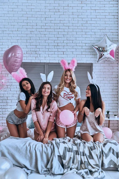 四顽皮的年轻微笑的妇女在兔子耳朵坐在床上与气球 — 图库照片