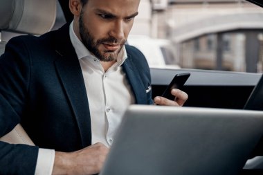 Kendine güvenen genç adam arabanın içinde otururken dizüstü kullanarak takım elbiseli