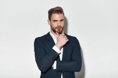 takım elbise ceket el çene ve kamera gri arka plan karşı dururken bakarak tutmak yakışıklı genç adam
