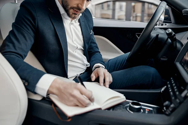 車の中に座って手帳にメモを書く完全なスーツの若者のクローズ アップ — ストック写真