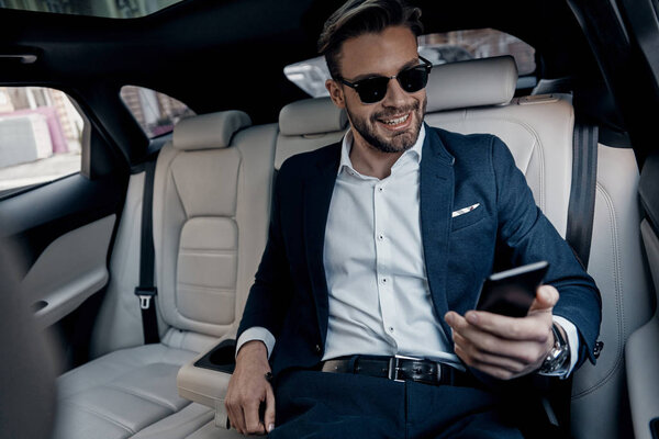 happy Handsome young businessman in suit looking at smart phone while sitting in car