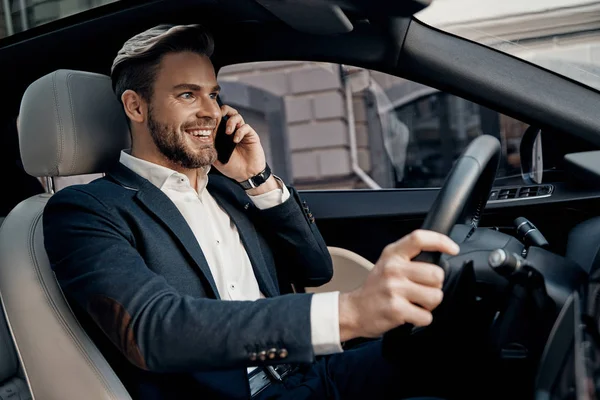 正式な摩耗彼のスマート電話で話していると高級車を運転している間笑顔でハンサムな若い男 — ストック写真