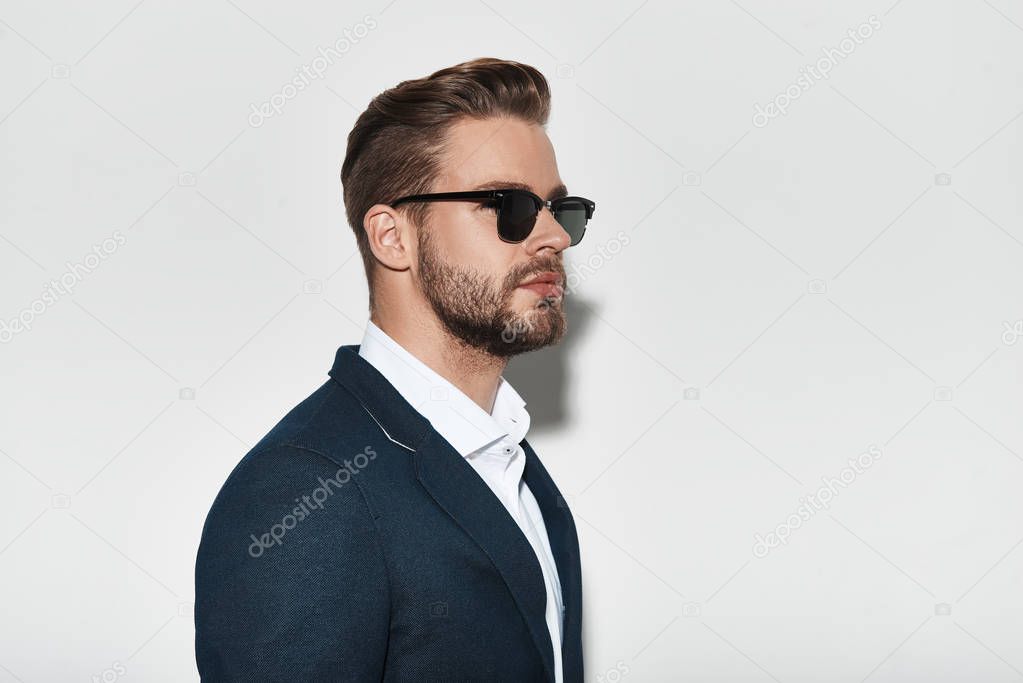Handsome young man in formal wear and sunglasses posing in studio