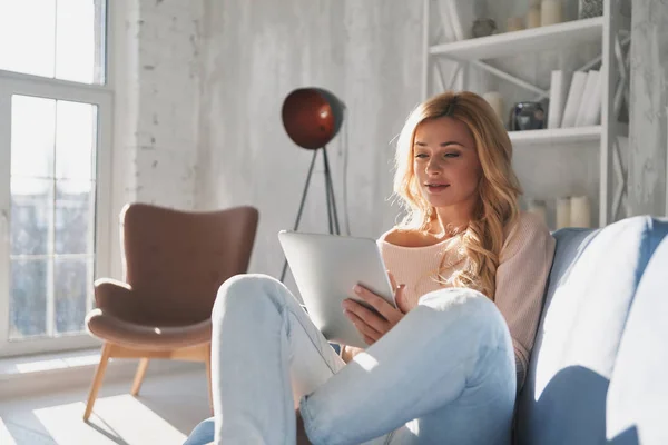 自宅でソファに座っている間 デジタルタブレットと笑顔を使用して魅力的な若い女性 — ストック写真