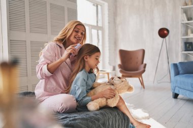 Güzel genç anne kızın saçlarını yatak odasında fırçalama