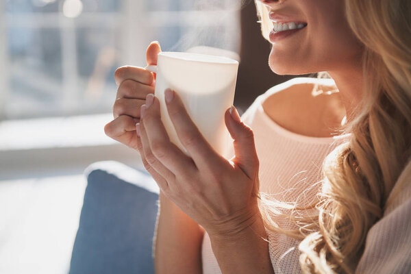 частичный вид молодой женщины, держащей чашку чая и улыбающейся дома
