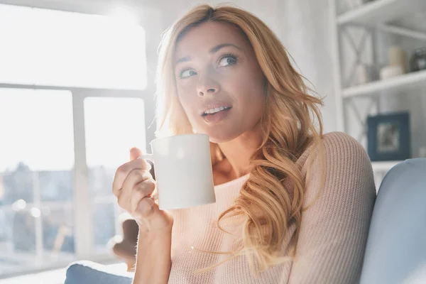 有魅力的年轻女子抱着杯子 看着一边在家里花时间 — 图库照片