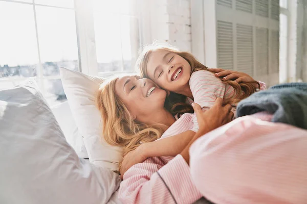 年轻美丽的母亲与逗人喜爱的小女儿微笑 当躺在床上在家 — 图库照片