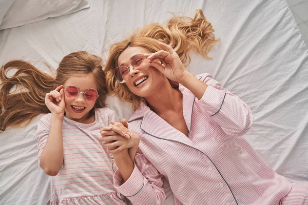 幸福美丽的母亲和可爱的女儿调整太阳眼镜和微笑 而躺在床上 — 图库照片