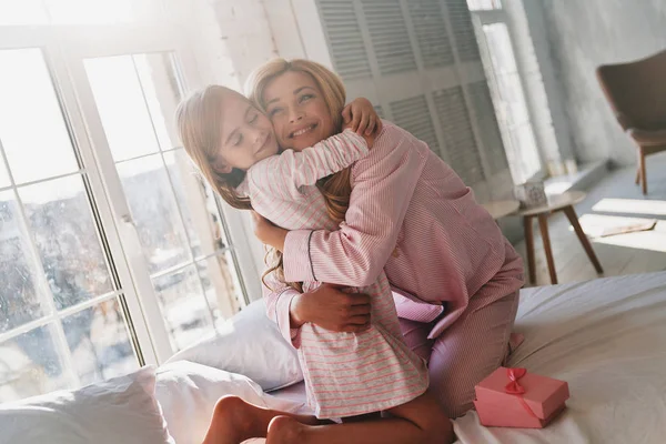 Linda Niña Abrazando Madre Mientras Está Sentada Cama Casa — Foto de Stock