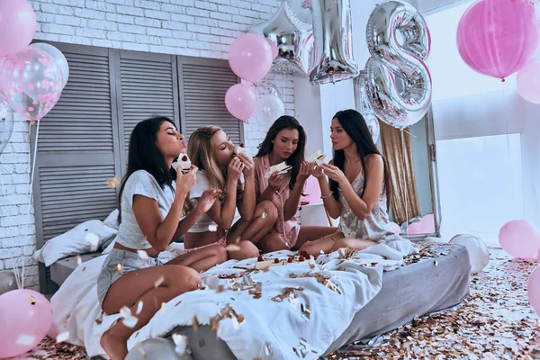 四美丽的年轻妇女穿着睡衣在卧室里吃蛋糕 里面有气球和五彩纸屑 — 图库照片