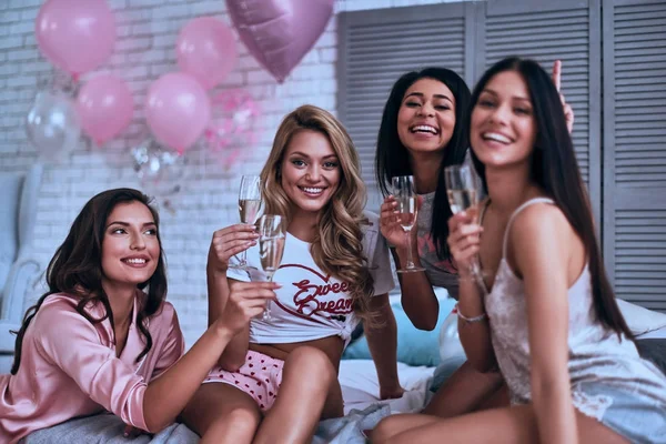 四美丽的年轻微笑的妇女在睡衣拿着香槟杯子和庆祝未婚女子党在卧室 — 图库照片