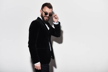 Onun gözlük ayarlama ve gri arka plan karşı dururken gülümseyen tam takım yakışıklı genç adam