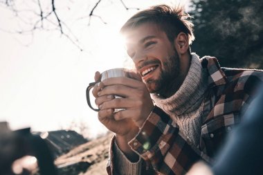 genç adam sabah içki sonbahar dağda kamp sırasında sıcak sıcak gri süveterli gülümseyen