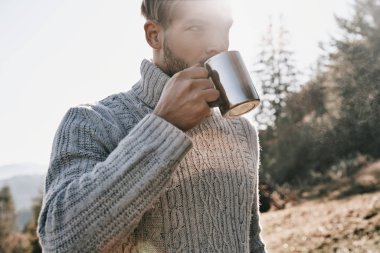 Yakışıklı genç sıcak gri süveterli sabah sıcak sonbahar dağda kamp sırasında içme