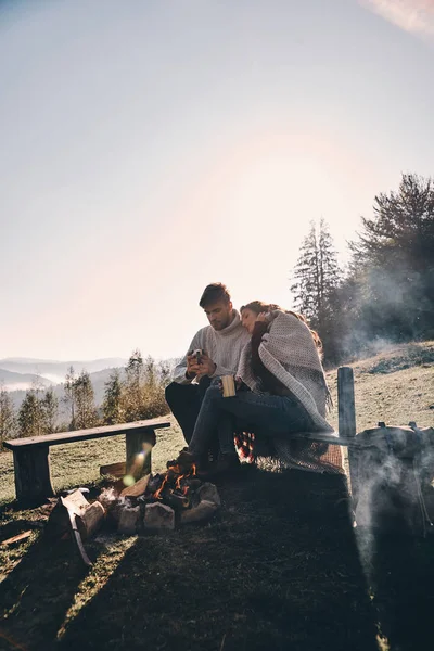 couple in love having hot drinks while spending carefree time in mountains near bonfire