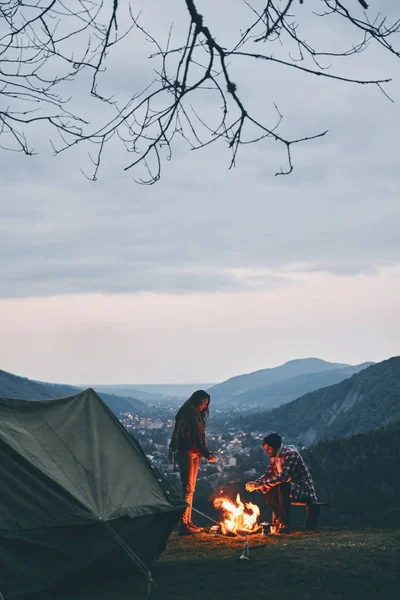 Casal Jovem Bonito Aquecendo Perto Fogueira Enquanto Acampando Nas Montanhas — Fotografia de Stock