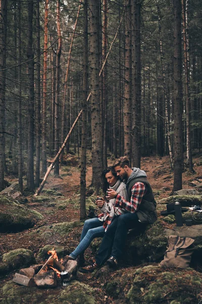 美丽的年轻情侣捧着杯子在森林里取暖的篝火旁 — 图库照片