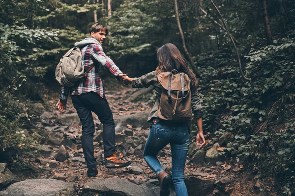 young couple holding hands and moving up while hiking together in woods