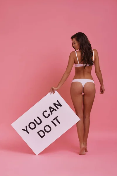 stock image Full length rear view of attractive young woman with perfect buttocks holding poster while standing on tiptoe against pink background