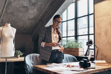 Onun atölyesinde masanın yanında dururken akıllı telefon kullanarak Eyewear çekici genç kadın